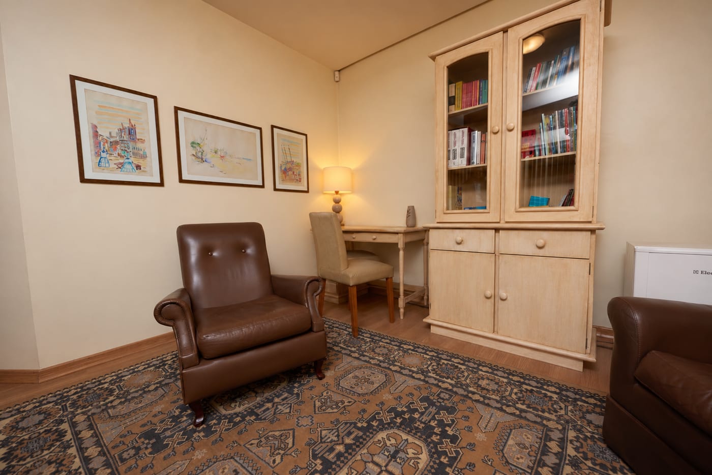 Consultório no Bom Fim, vazio e pronto para atender: duas poltronas de couro, quadros na parede, mesa com luminária e armário de madeira com livros